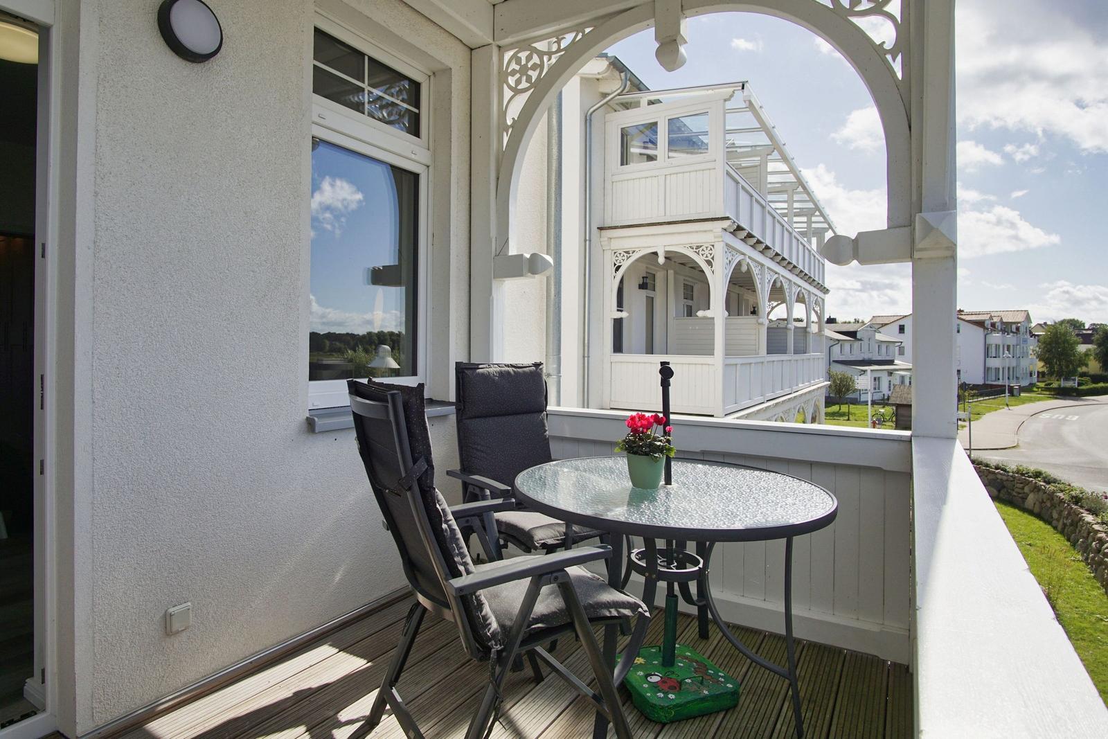 Terrasse mit Tisch und zwei Stühlen, Blick auf weiße Veranda und Straße.