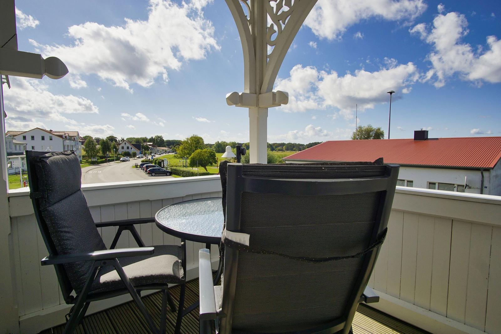 Terrasse mit zwei Stühlen und Tisch. Blick auf Straße und Gebäude.
