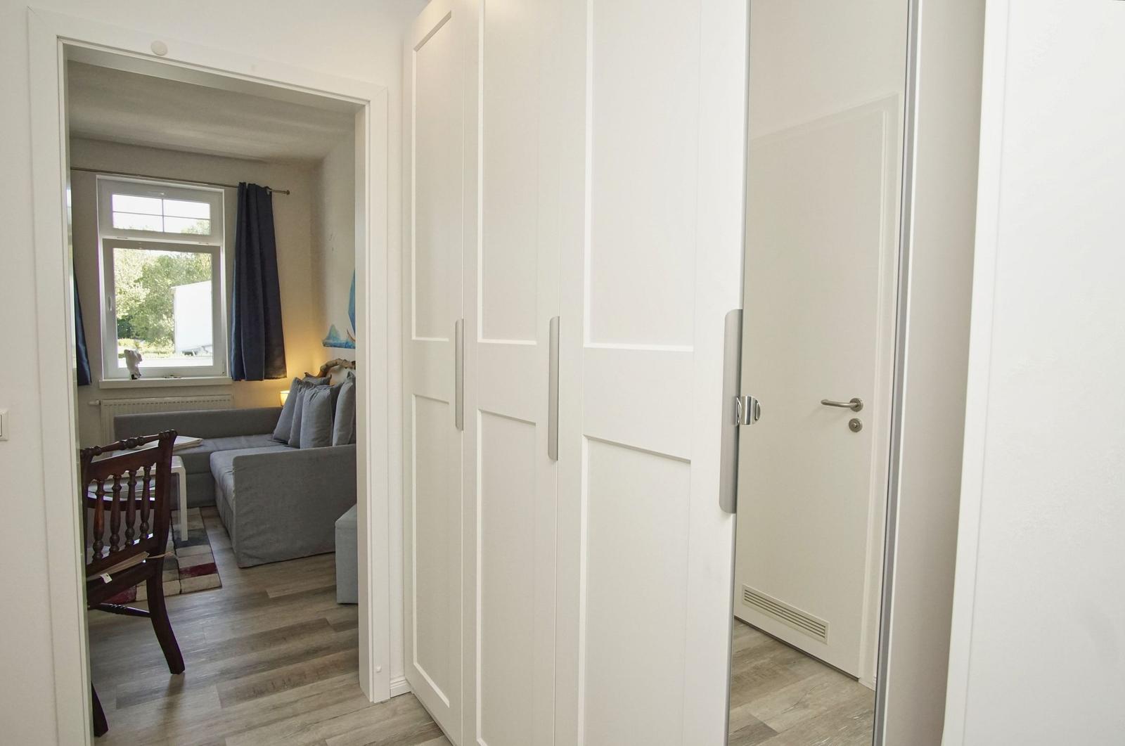 Hallenflur mit weißen Schränken und Blick in Wohnbereich mit Sofa und Fenster.