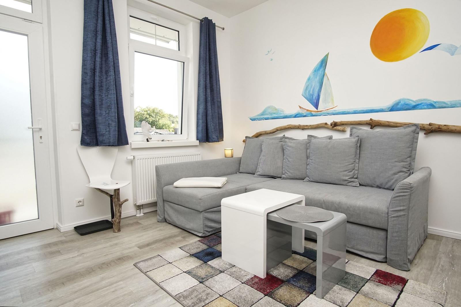 Wohnzimmer mit grauem Sofa, blauen Vorhängen und Wandmalerei mit Segelboot.