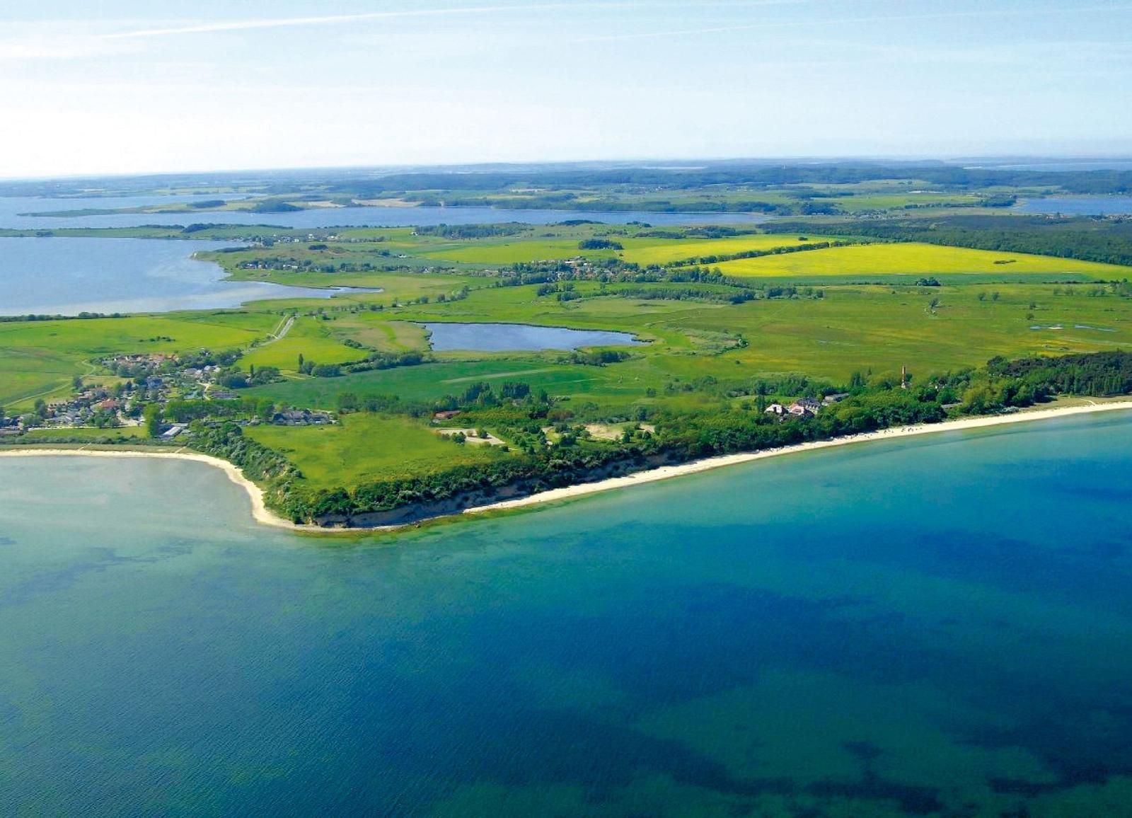 Aerial view of coastal landscape with green fields, lakes, and sandy beach.