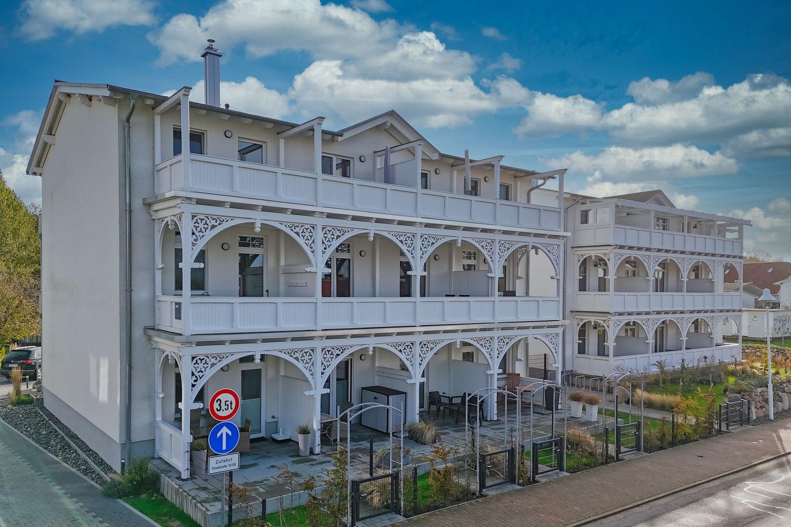 Weiße Ferienwohnung mit Balkonen und Gartenbereich unter blauem Himmel.
