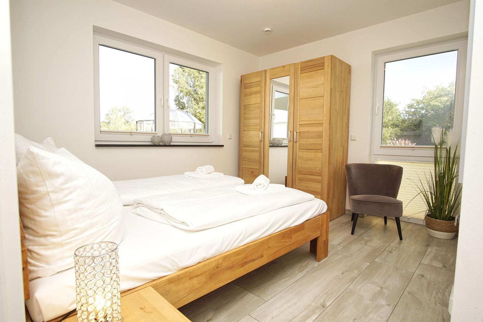 Schlafzimmer mit Holzbett, Kleiderschrank und Fenstern mit Blick auf Garten.