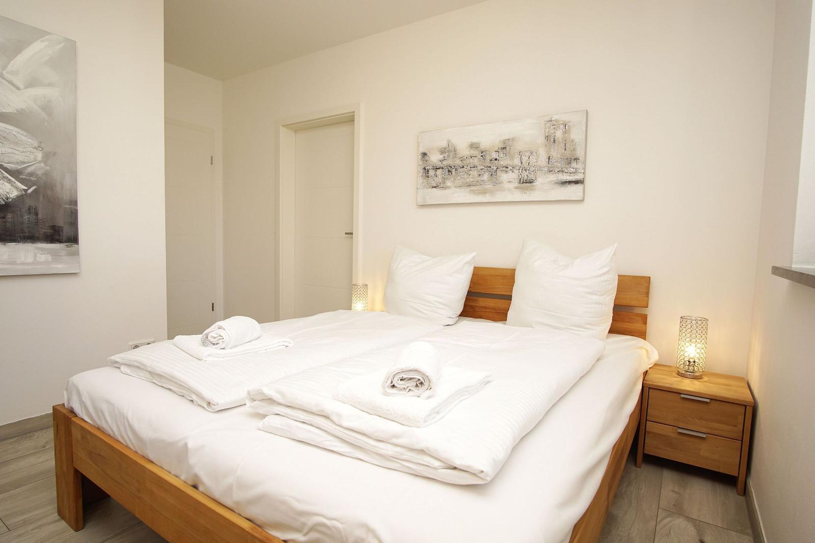 Schlafzimmer mit Doppelbett, Holzgestell und Nachttisch mit Lampe.