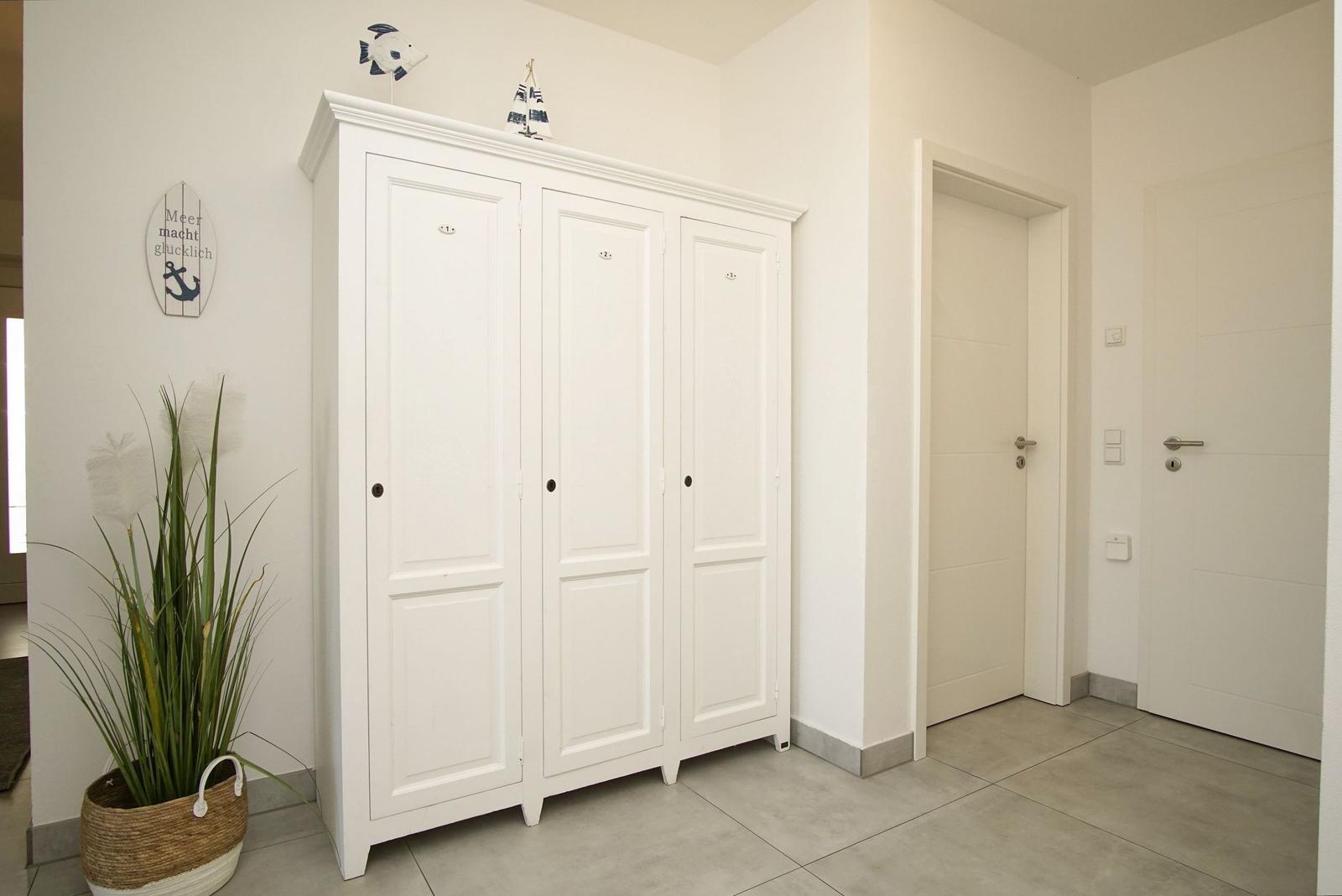 Eingangsbereich mit weißem Schrank, Pflanze und Wanddekoration.