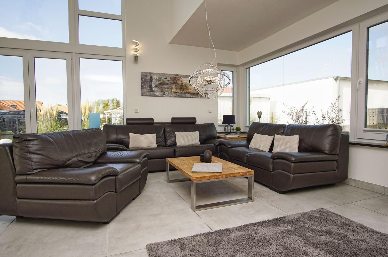 Großes Wohnzimmer mit braunen Ledersofas, Holztisch und großflächigen Fenstern.