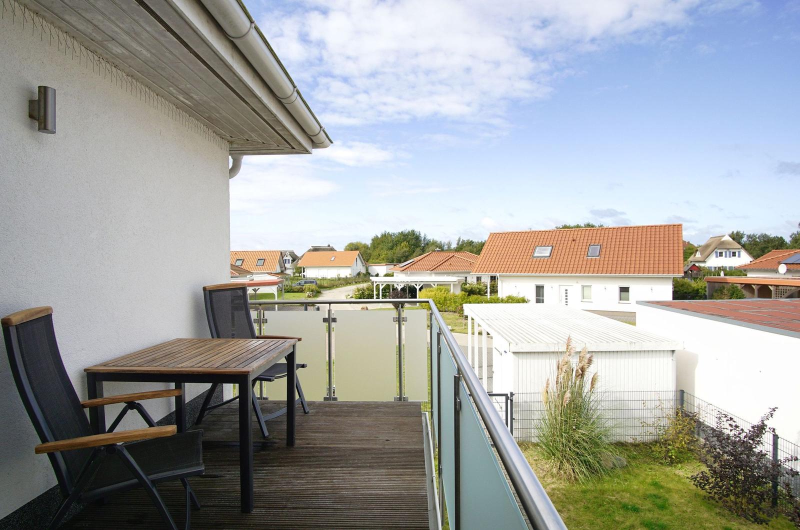 Terrasse mit Tisch und Stühlen, Blick auf Wohnhäuser und Grünflächen.