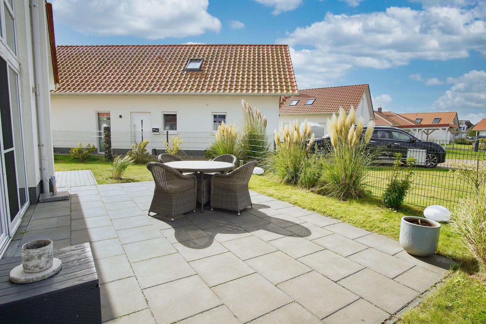 Terrasse mit Sitzgruppe, Garten und Nachbarhäuser unter blauem Himmel.