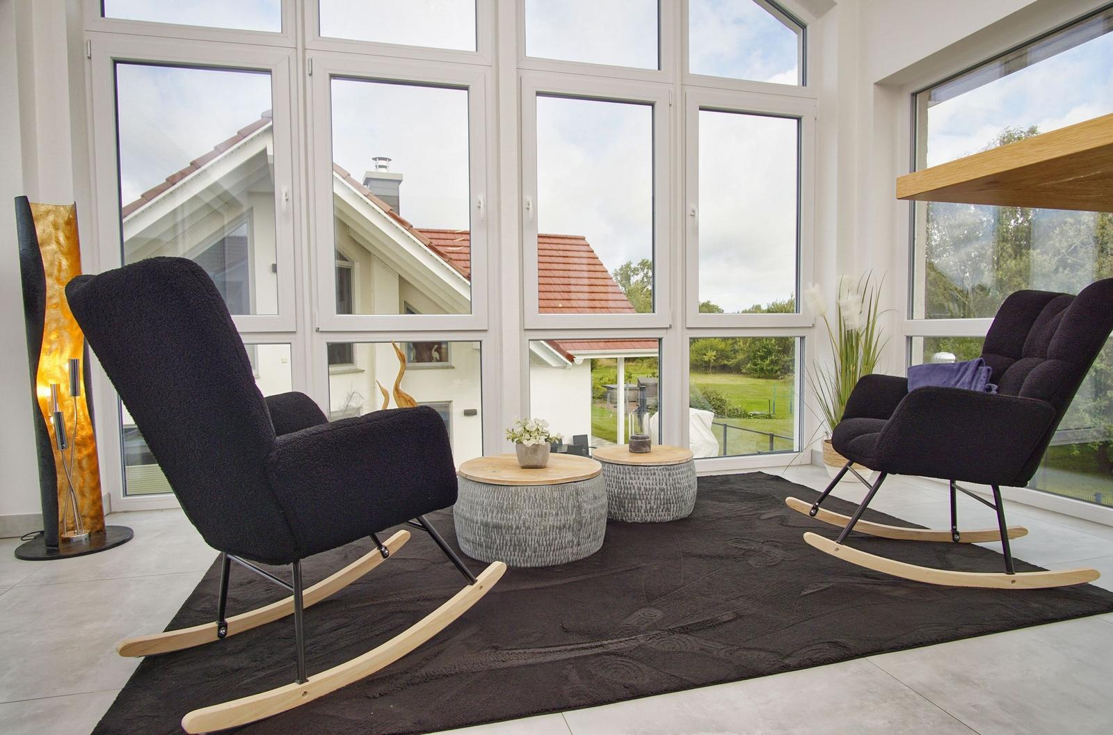 Zwei schwarze Schaukelstühle stehen auf einem dunklen Teppich vor großen Fenstern.