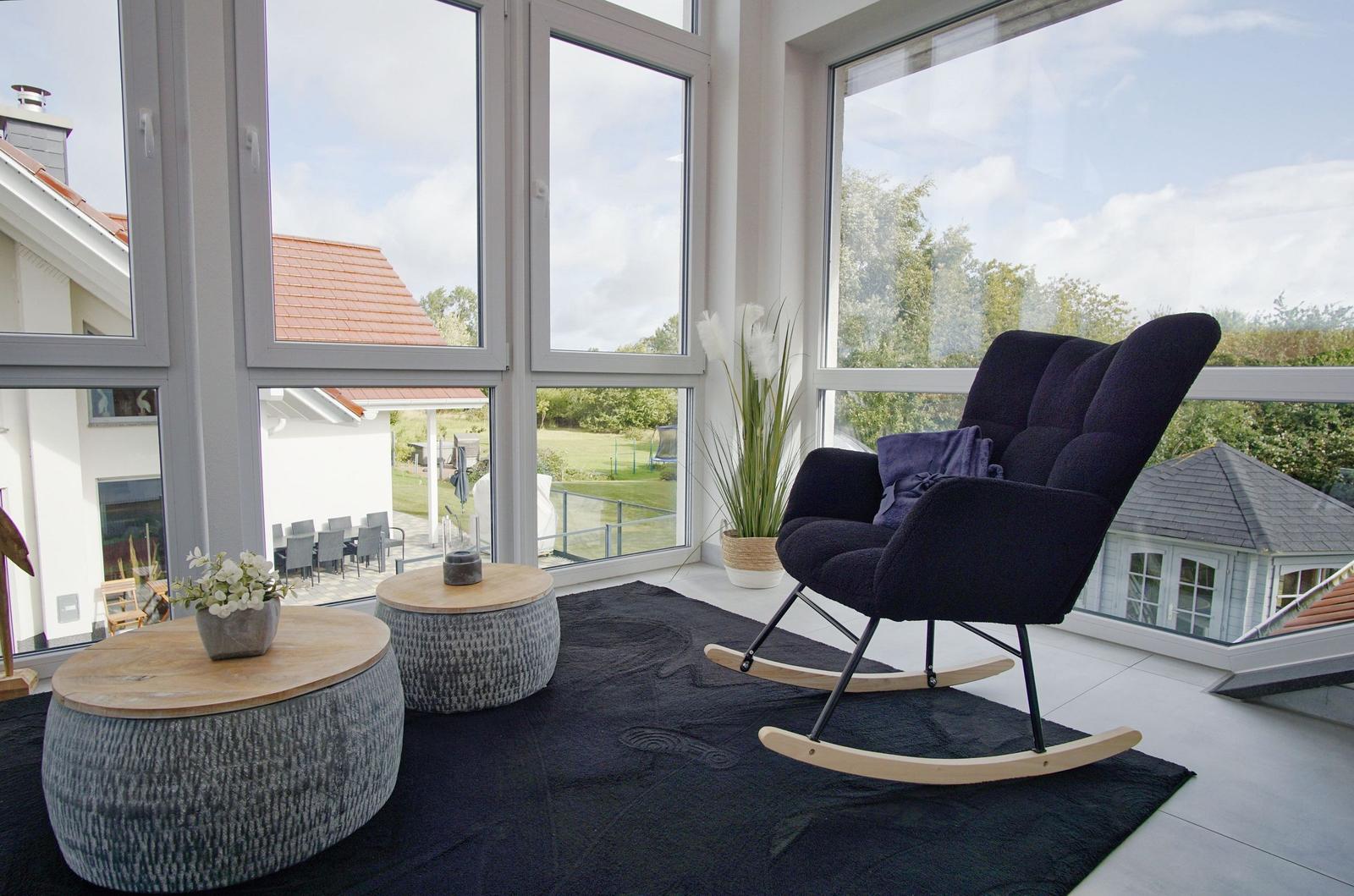 Ein Raum mit großem Fenster, Schaukelstuhl und zwei runden Tischen.