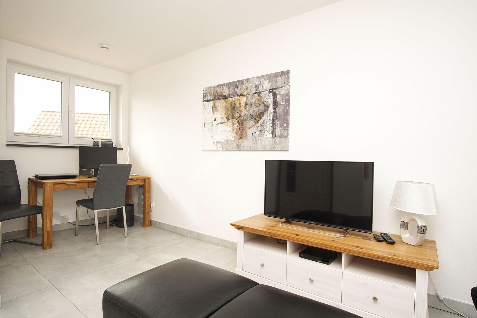 Wohnzimmer mit TV, Schreibtisch und Fenster. Wandbild und Beistelltisch.