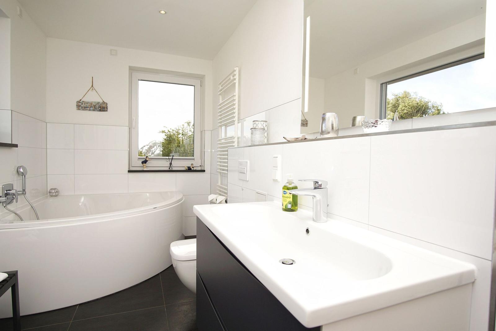 Badezimmer mit Badewanne, Waschtisch und Fenster mit Blick auf Grün.