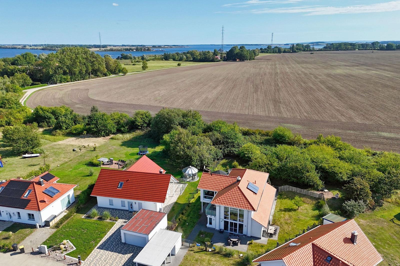 Haus mit rotem Dach und Garten, umgeben von Feldern und einem See.