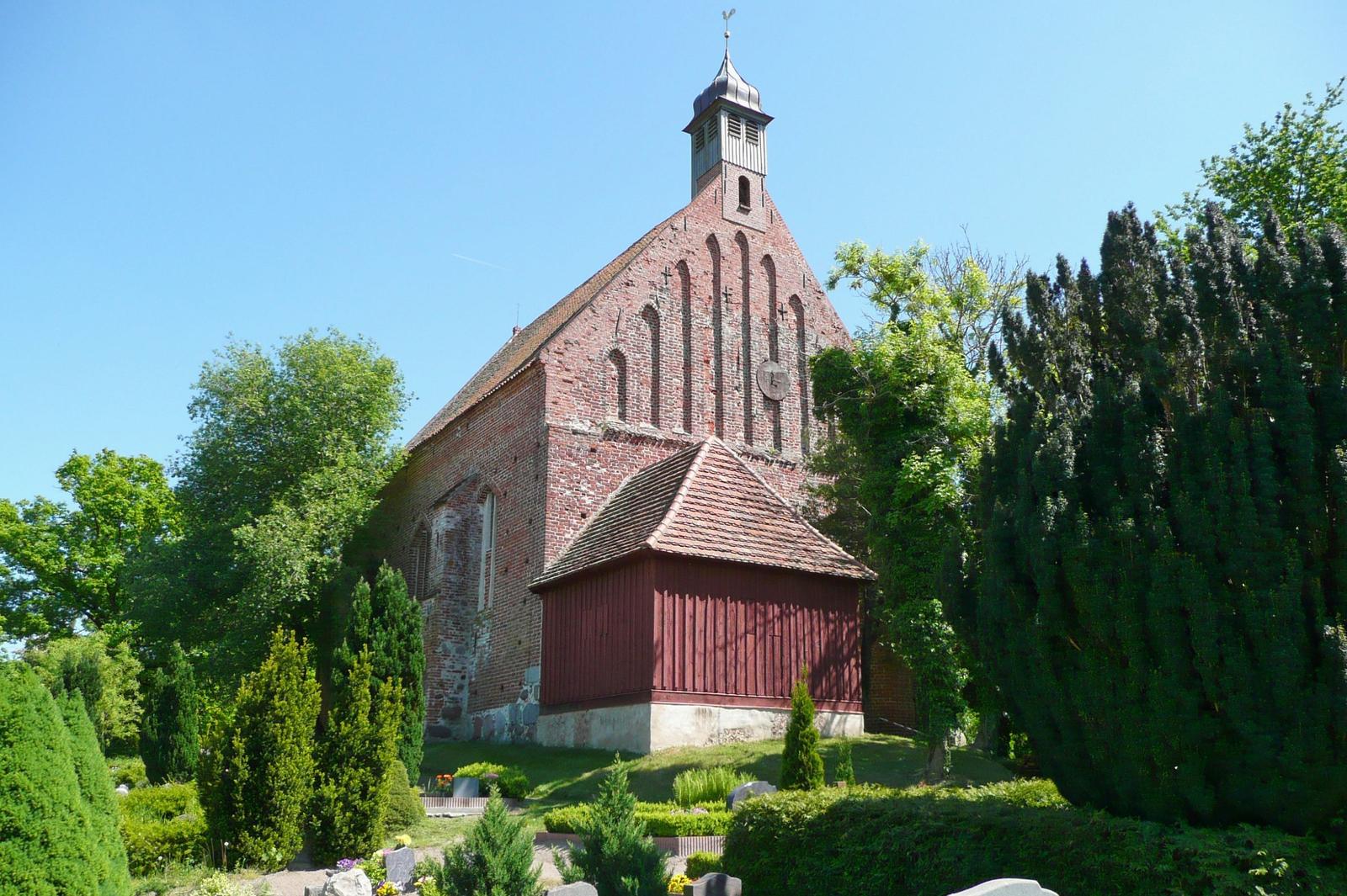 Historische Kirche mit rotem Dach und umliegenden Bäumen.