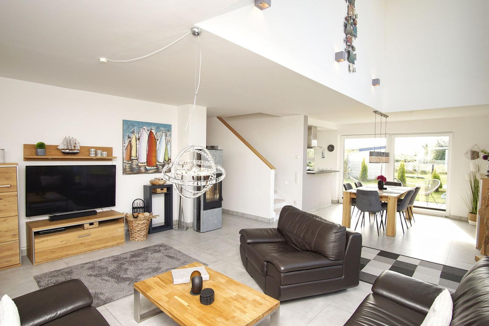 Wohn- und Essbereich mit Sofa, TV und Tisch. Durchgang zur Küche und Terrasse.