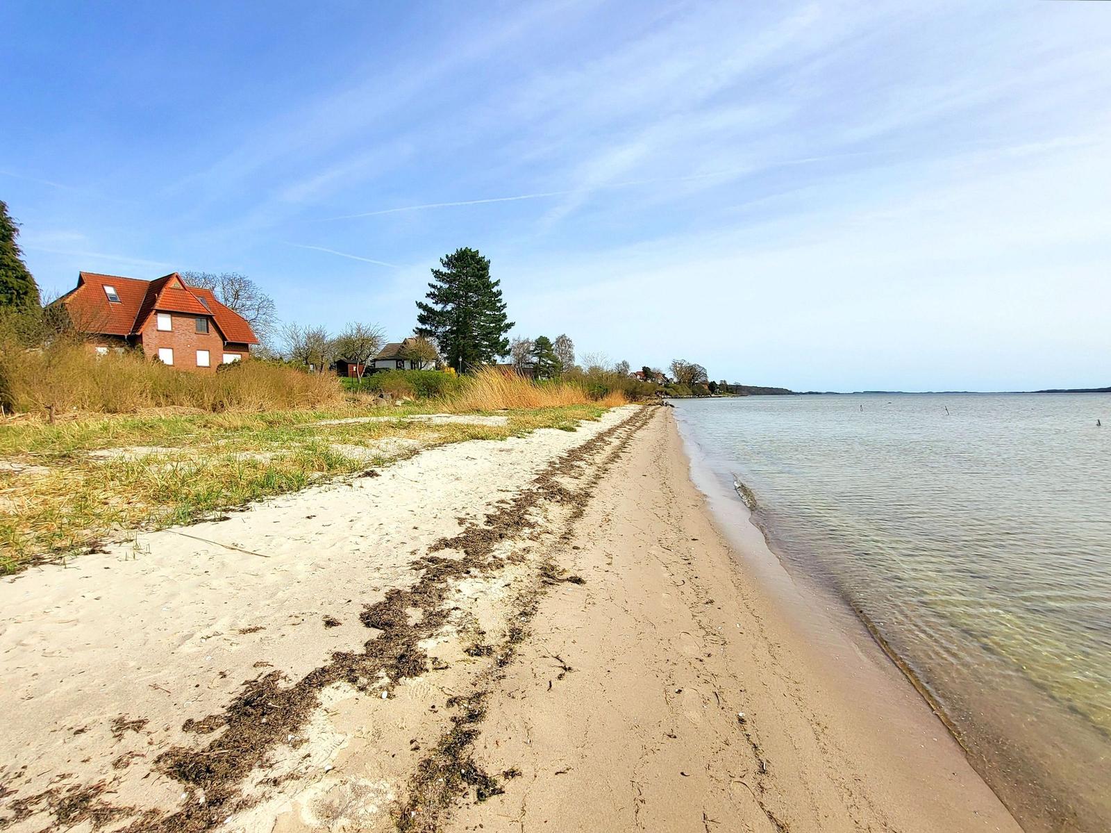 Strand mit Sand, Gras und Häusern am Wasser