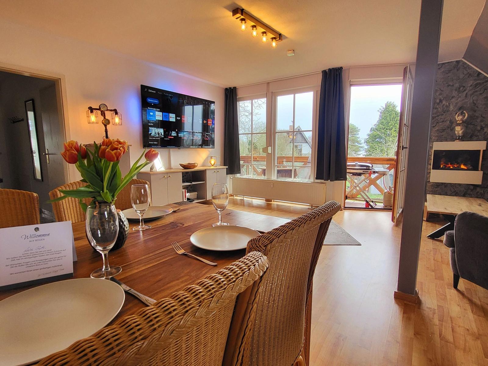 Esszimmer mit TV, Balkon und Kaminofen. Tisch gedeckt mit Tulpen.