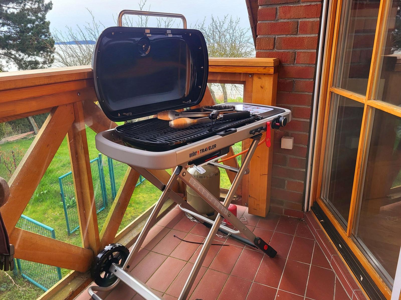 Grill steht auf Terrasse neben Hauswand mit Blick auf Garten.
