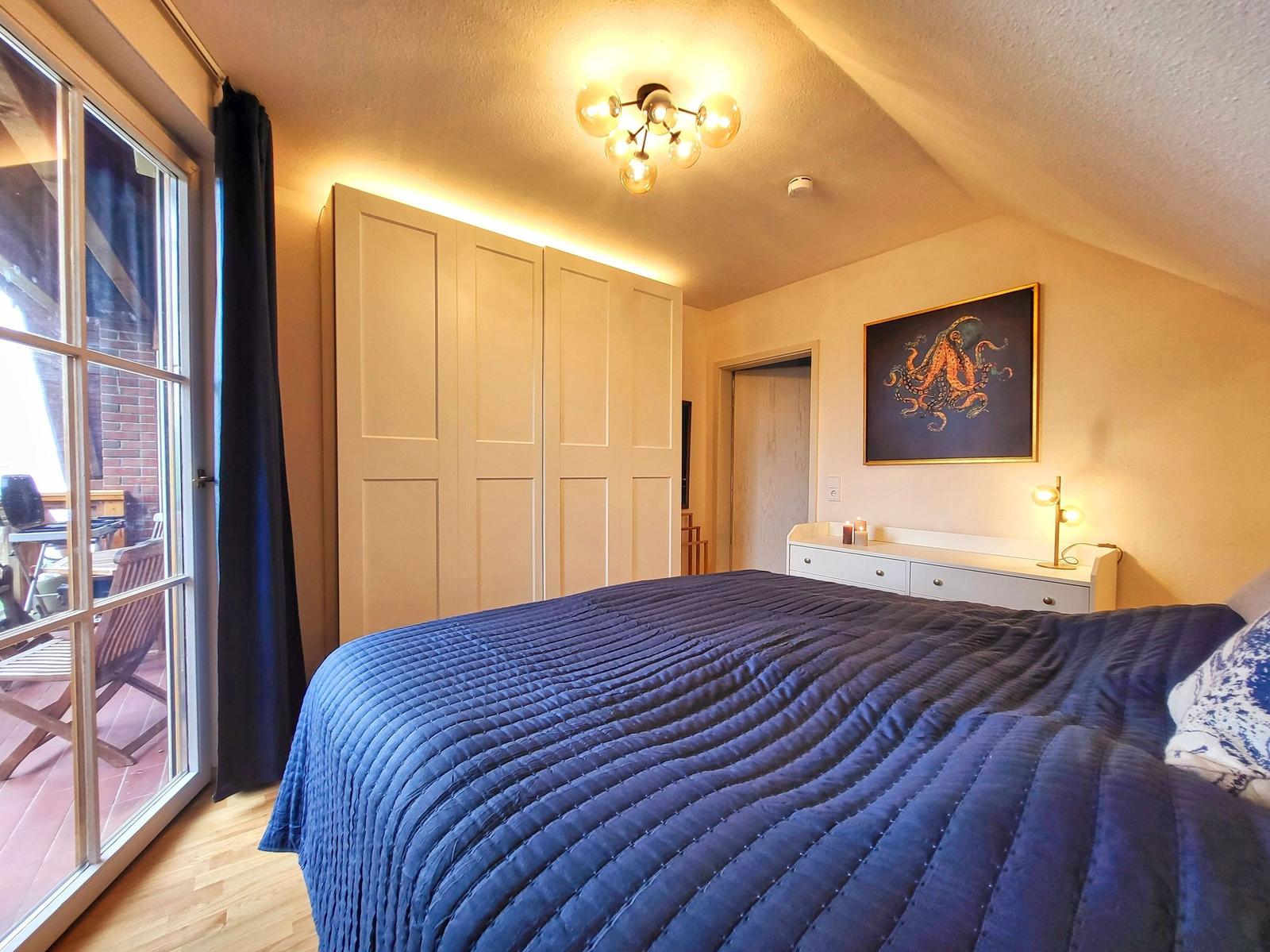 Schlafzimmer mit Bett, Kleiderschrank und Fenster zum Balkon.