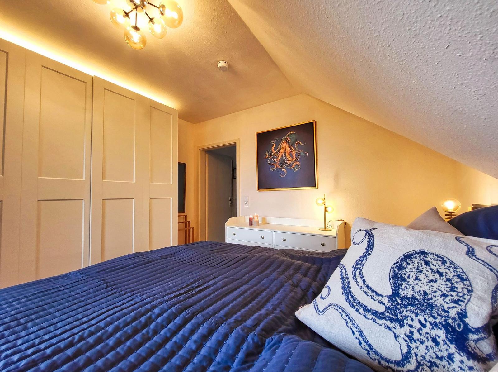 Schlafzimmer mit Bett, Kleiderschrank und Wandbild mit Oktopusmotiv.
