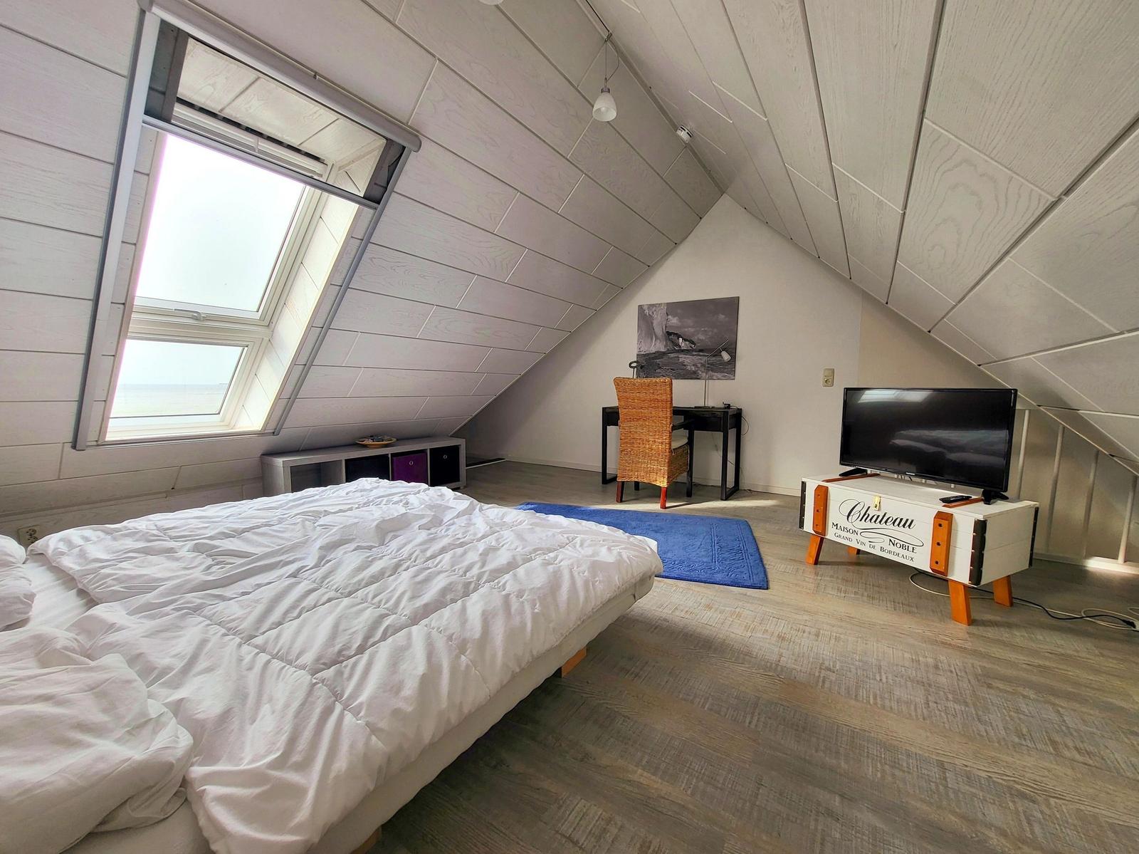 Schlafzimmer mit Dachfenster, Bett, Schreibtisch und TV.