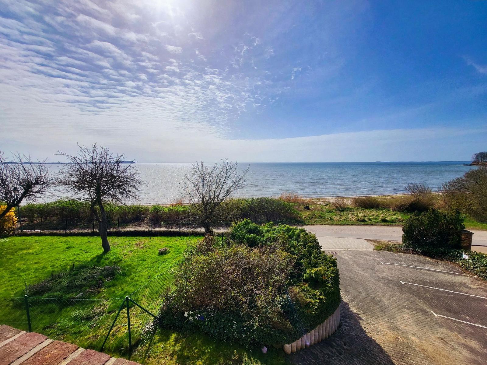 Meerfront mit Grünfläche und Parkplatz. Blick auf die Küste unter blauem Himmel.