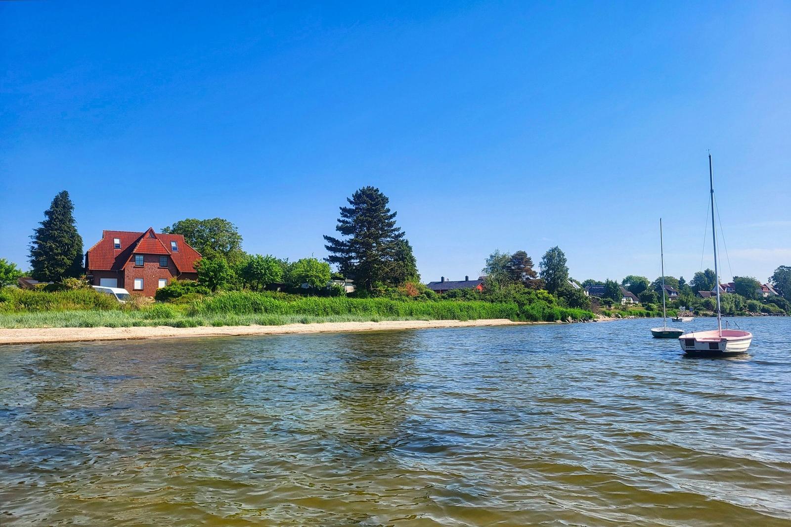 Haus am Wasser mit Segelbooten und grüner Umgebung.