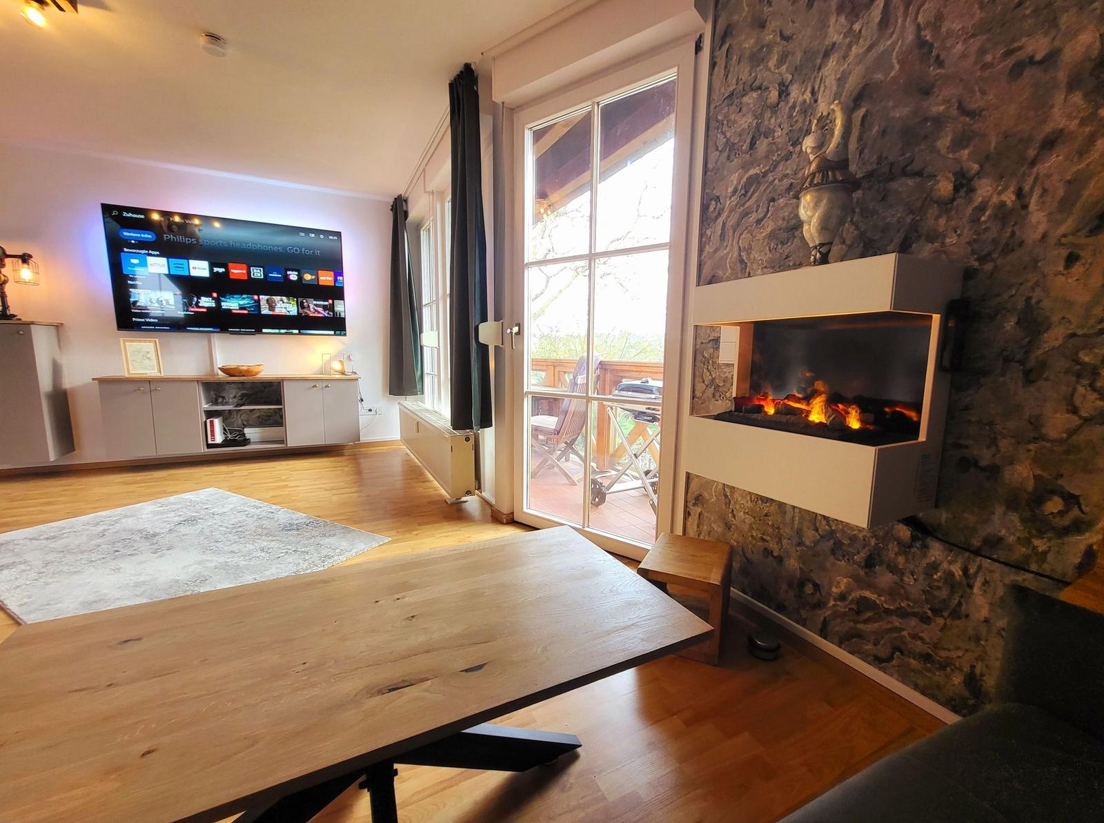 Wohnzimmer mit Kamin, TV und Terrasse.