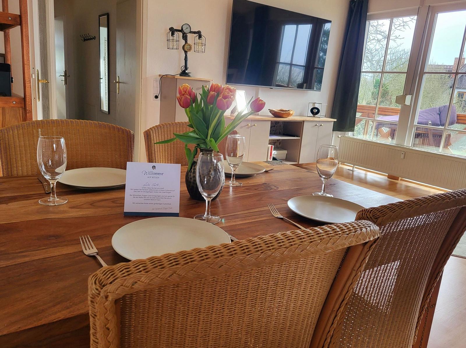 Esstisch mit Stühlen, Blumen und TV im Wohnbereich.