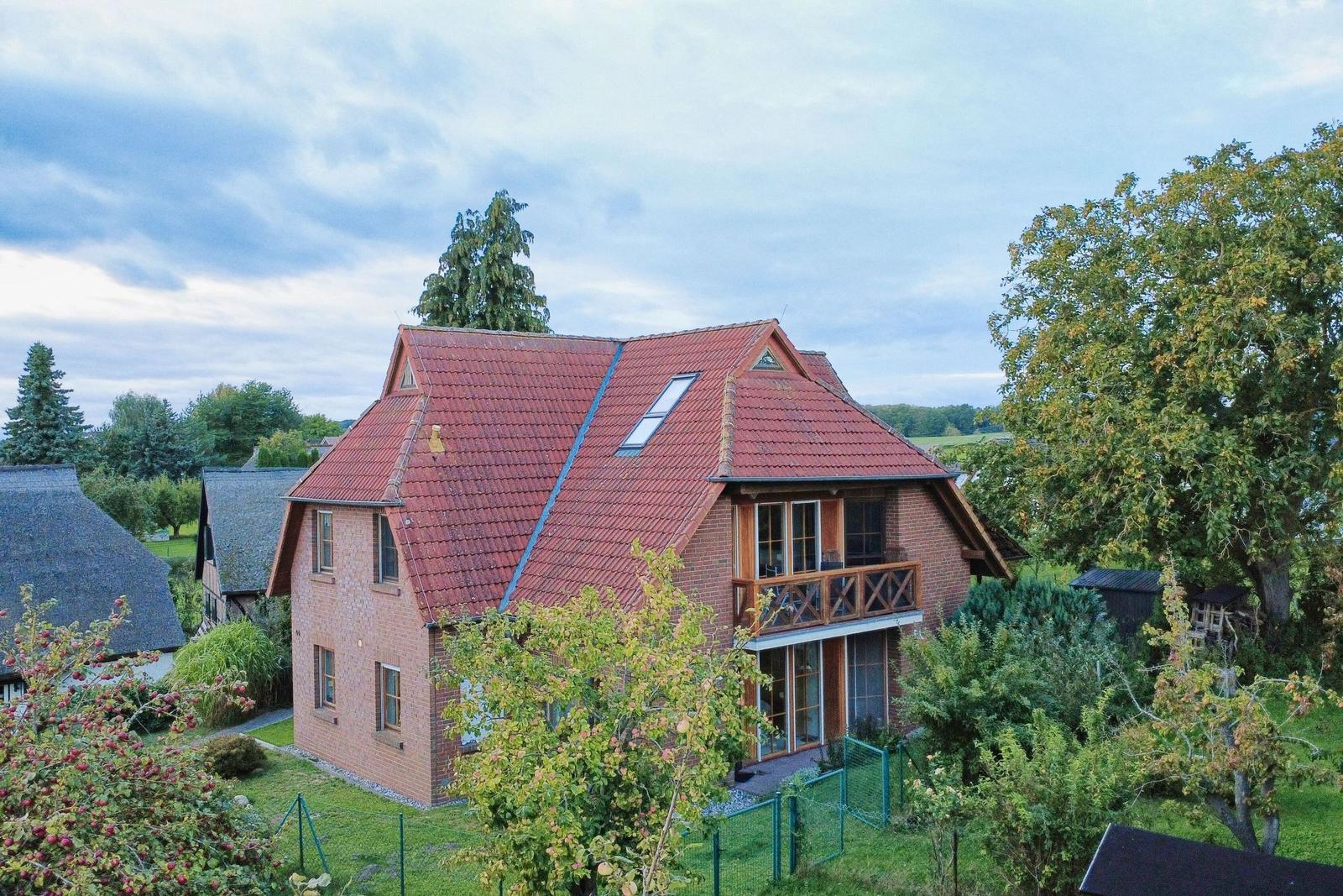 Zweistöckiges Haus mit rotem Dach und Balkon in grüner Umgebung.