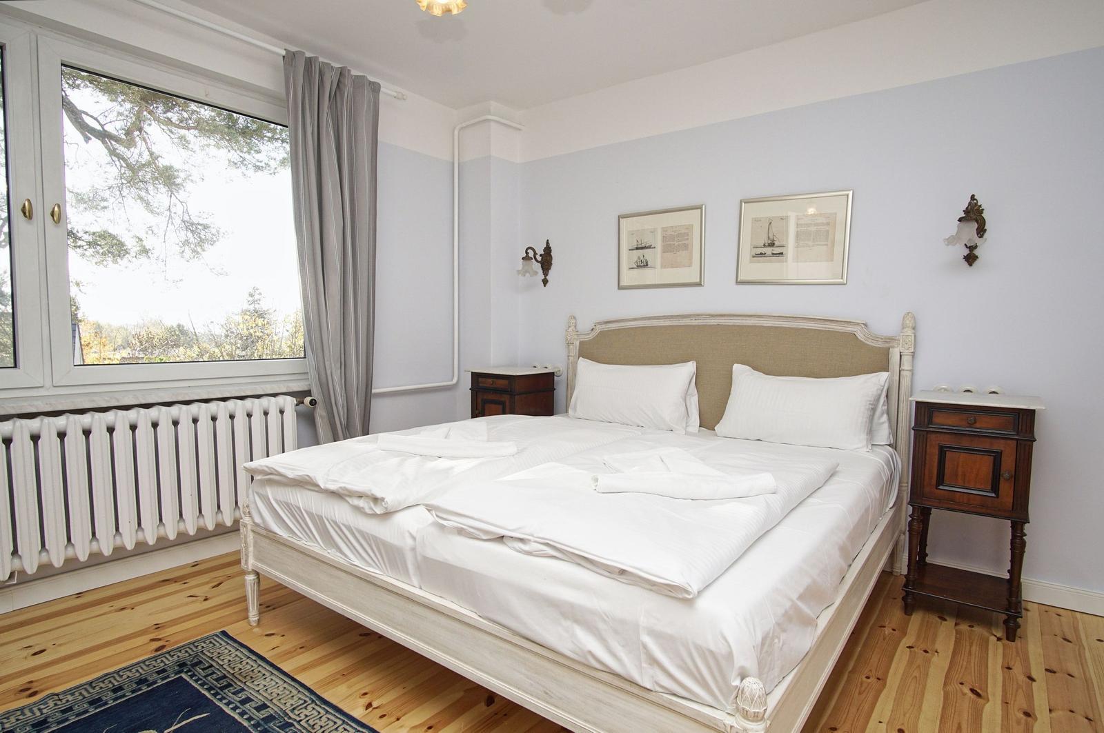 Schlafzimmer mit Doppelbett, Holzboden und Fensterblick auf Bäume.