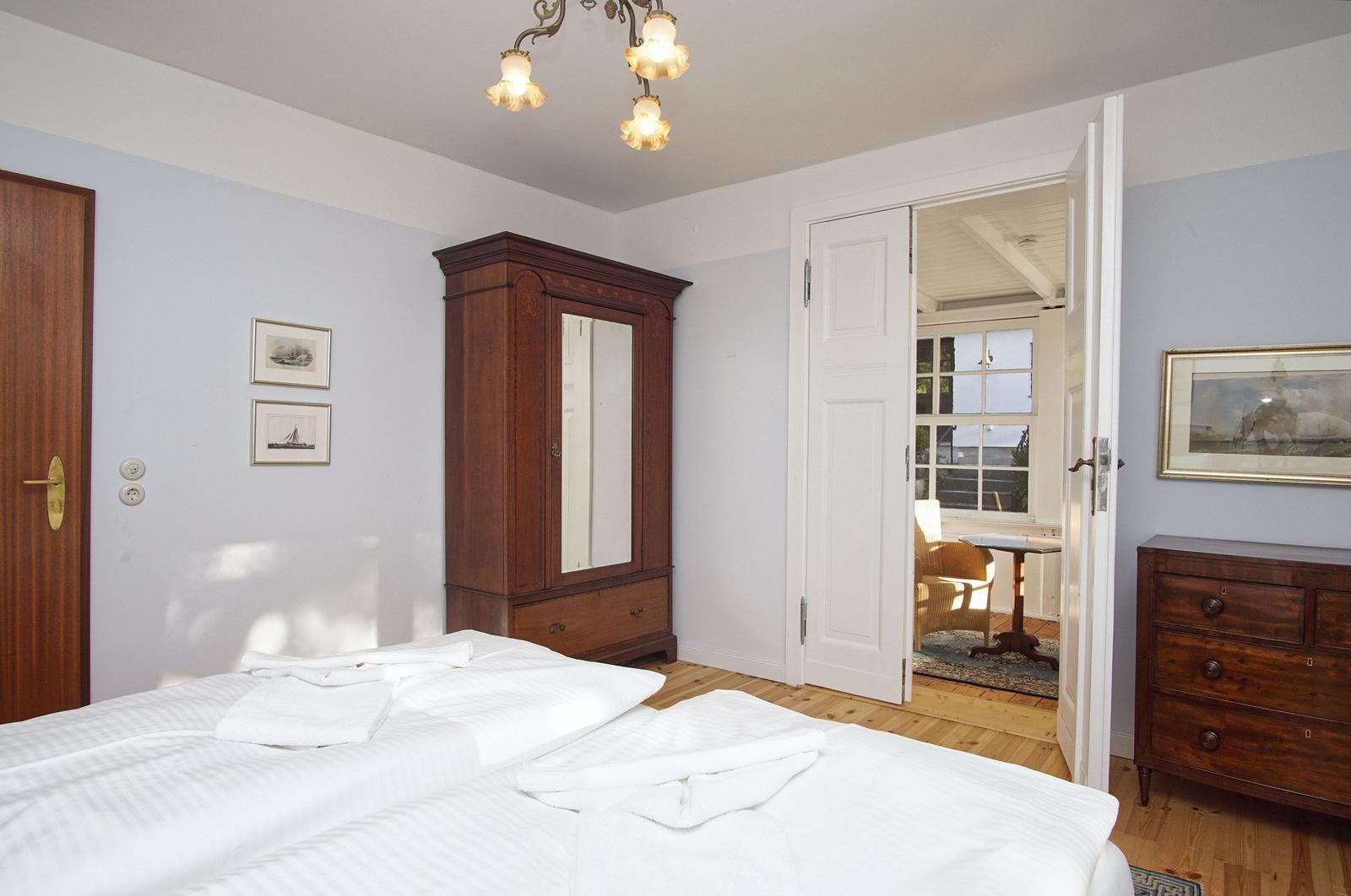 Schlafzimmer mit Bett, Kleiderschrank und Türen zu einem angrenzenden Raum.