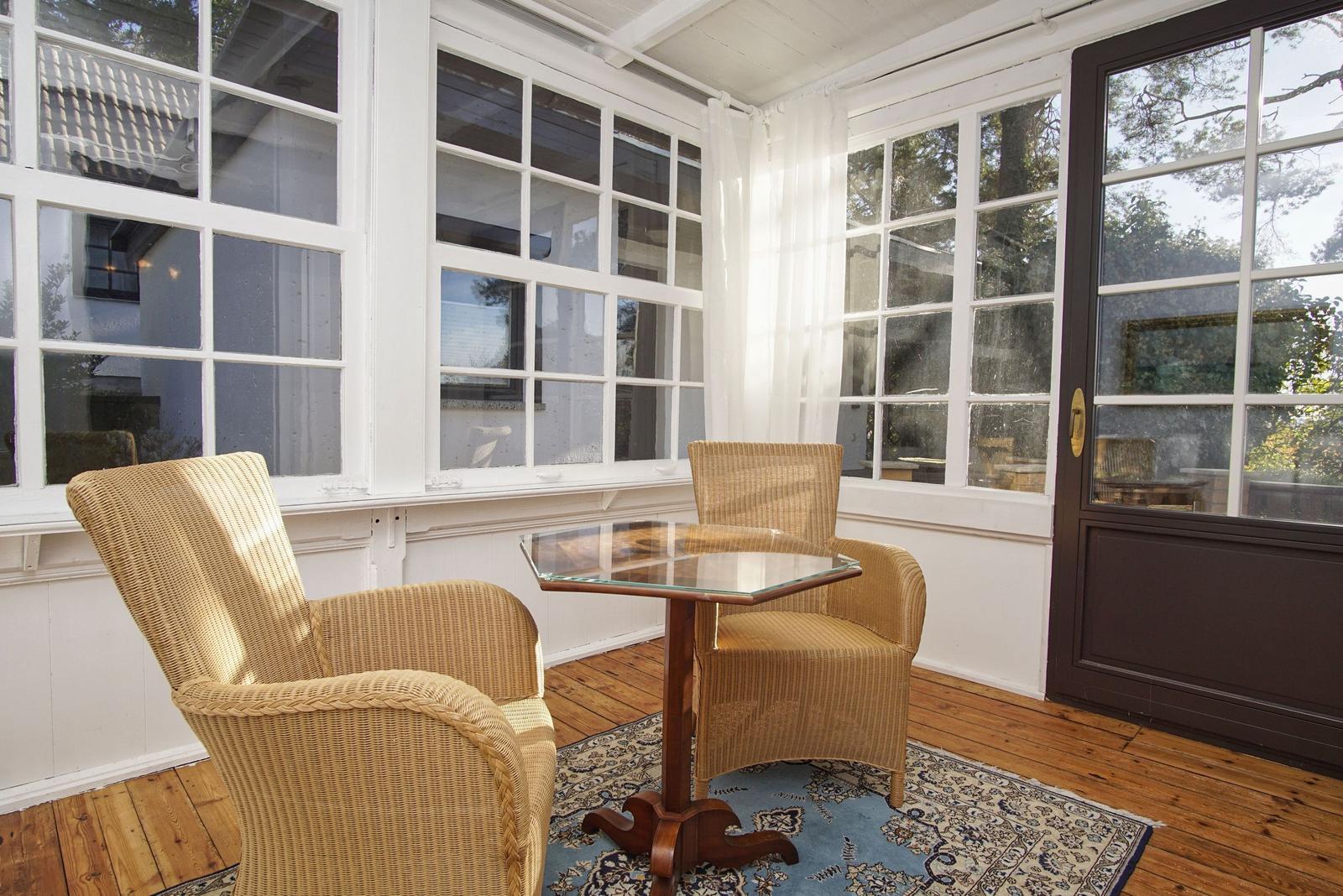 Terrasse mit zwei Rattanstühlen und Glas-Tisch auf Holzboden.
