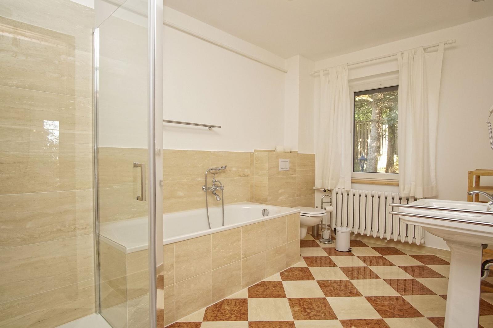 Badezimmer mit Badewanne, Dusche, Waschbecken und Fenster.