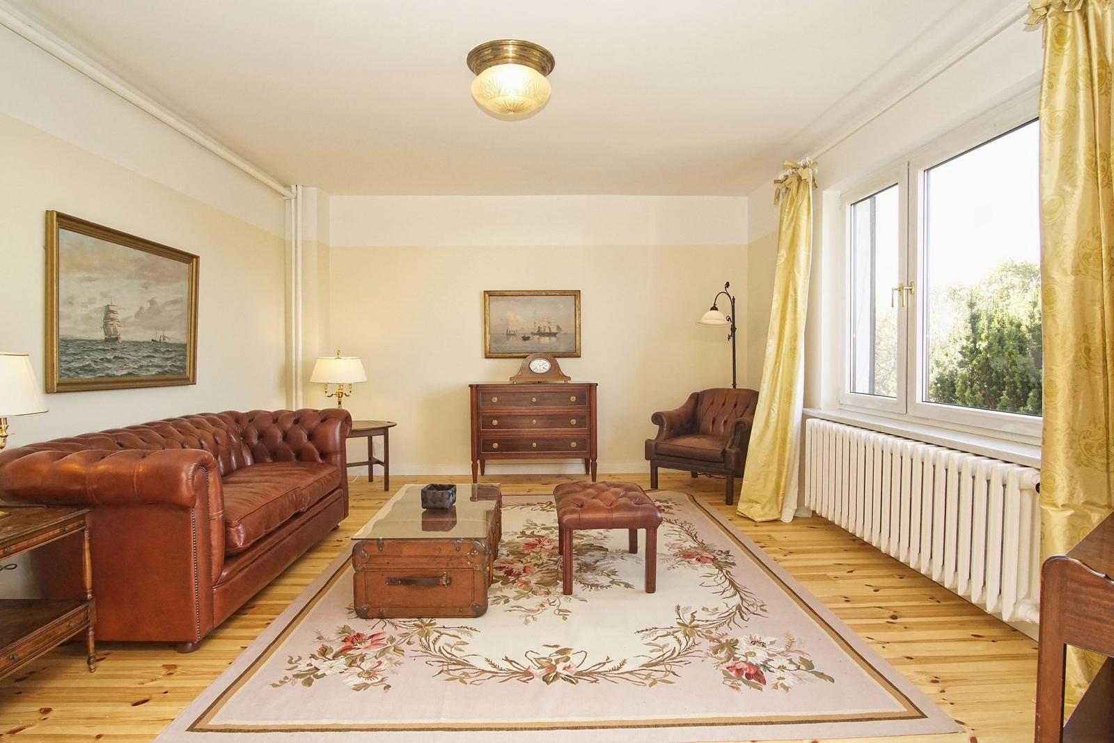 Wohnzimmer mit Ledersofa, Holzboden und Fenster mit Blick auf Grün.