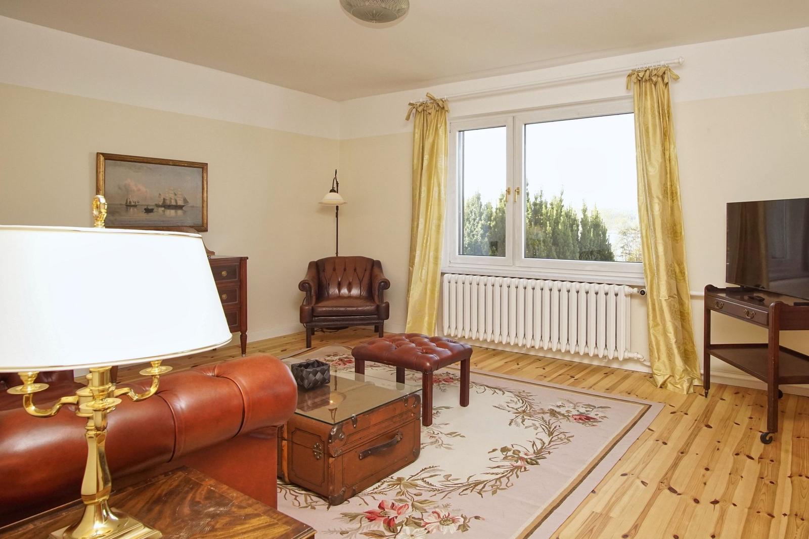 Wohnzimmer mit Ledersofa, Holzboden und Fenster mit gelben Vorhängen.