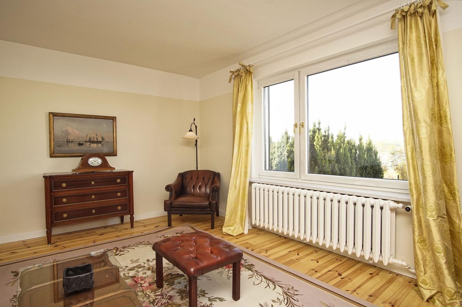 Raum mit braunem Ledersessel, Holzboden und Fenster mit goldfarbenen Vorhängen.