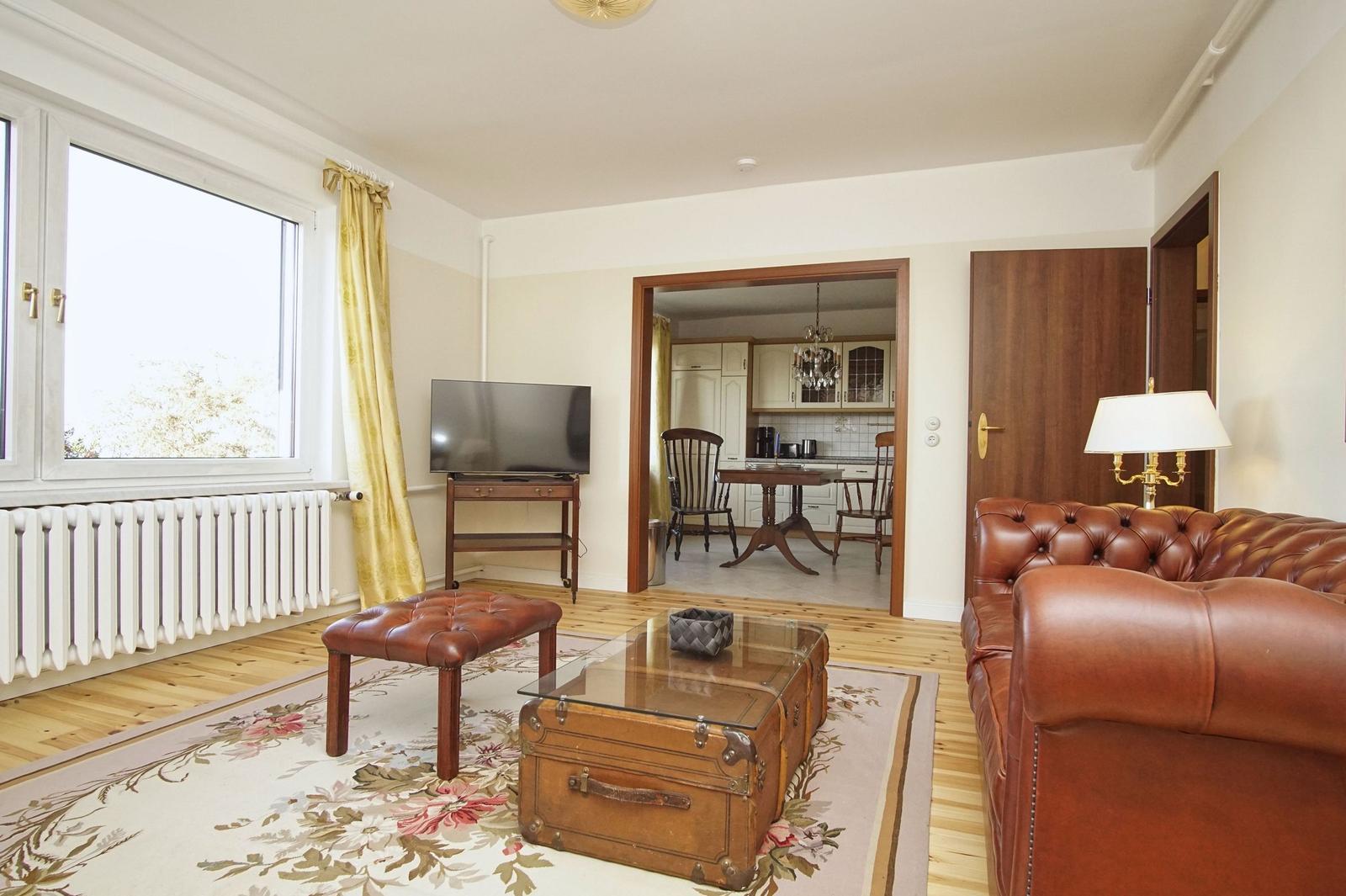 Wohnzimmer mit Ledersofa, Fernseher und Blick auf die Küche.