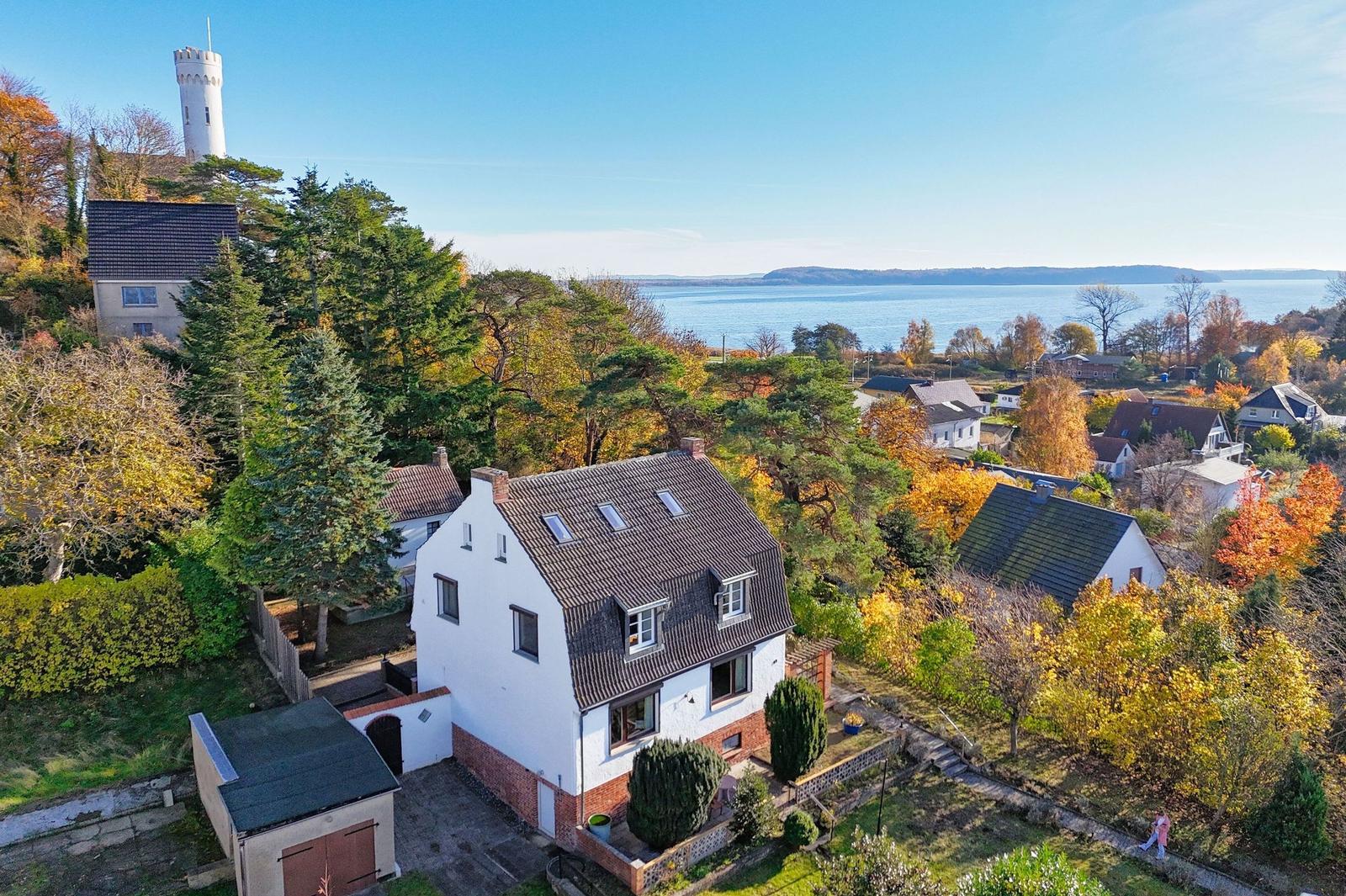 Wohnhaus mit Blick auf See und Turm, umgeben von Herbstbäumen.