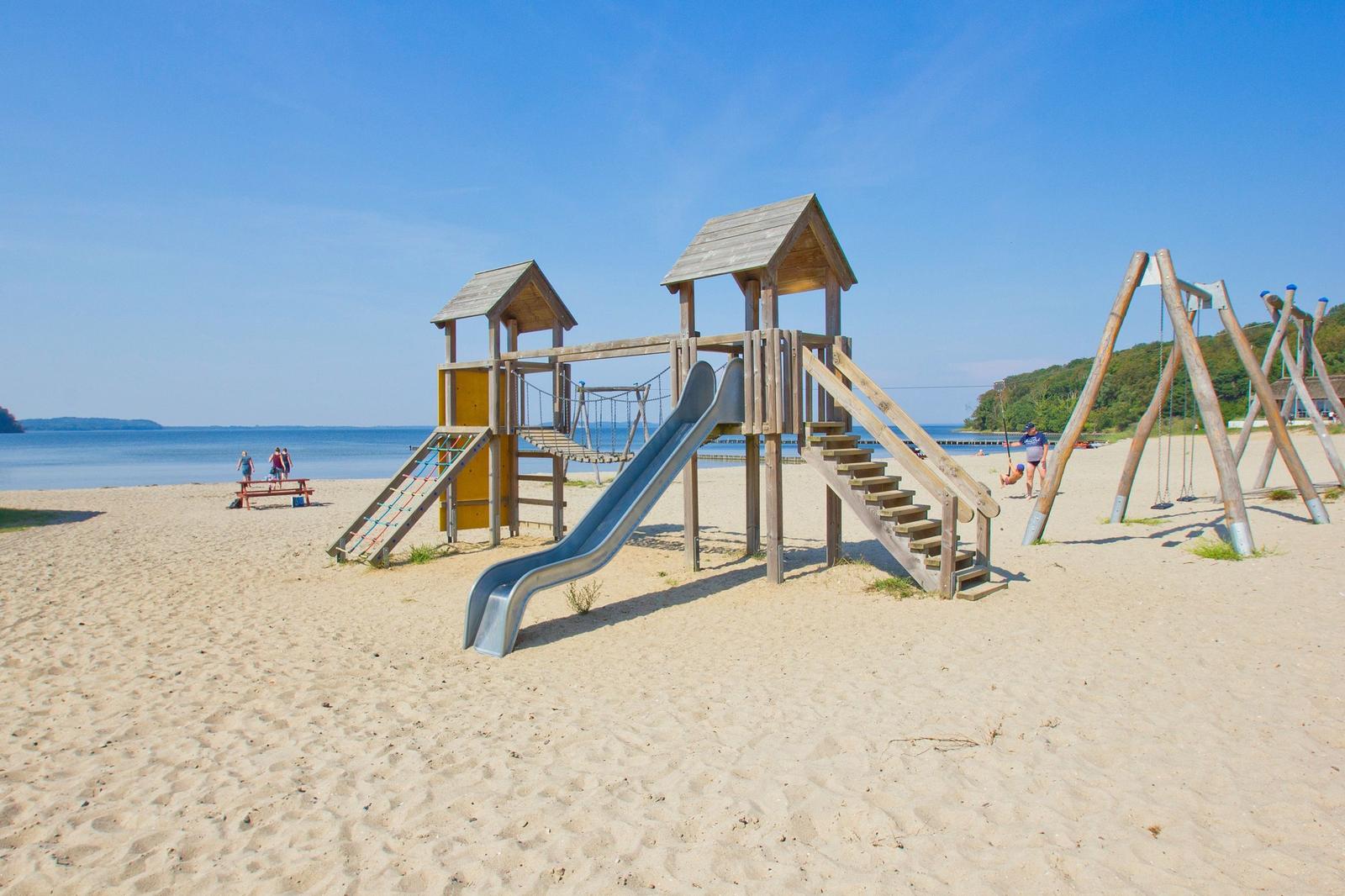 Große Sandstrandspielanlage mit Rutsche und Schaukel nahe Wasser.