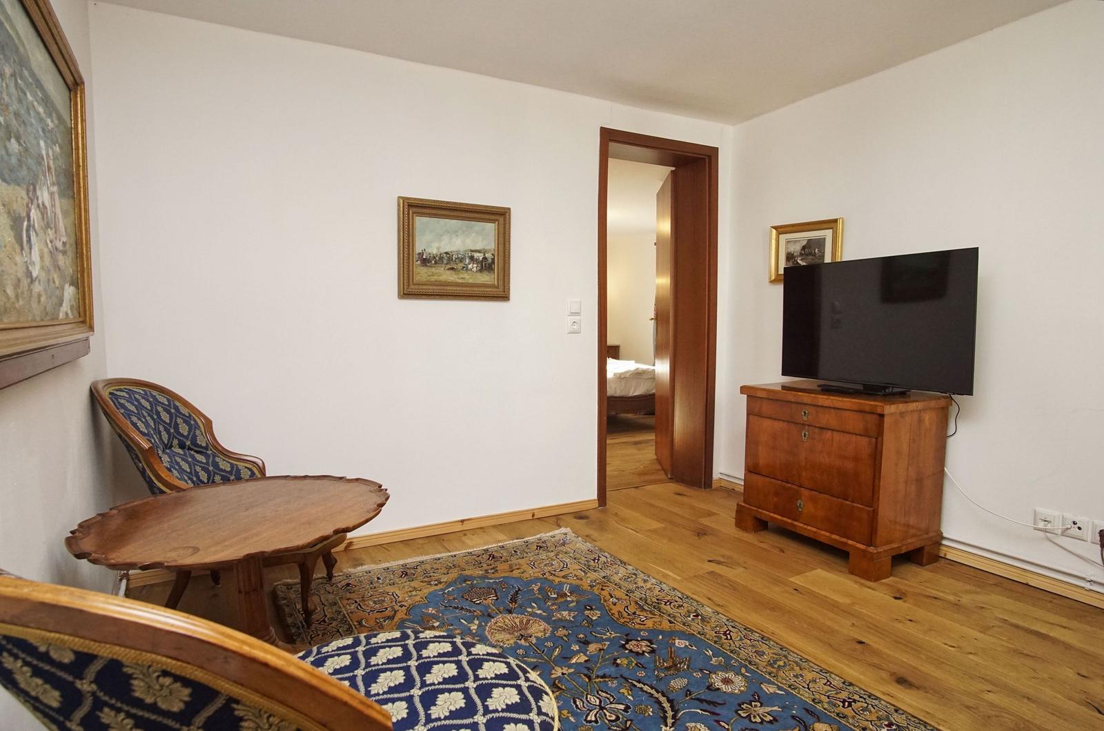 Wohnzimmer mit Holzboden, Teppich, TV und Sitzgelegenheit.