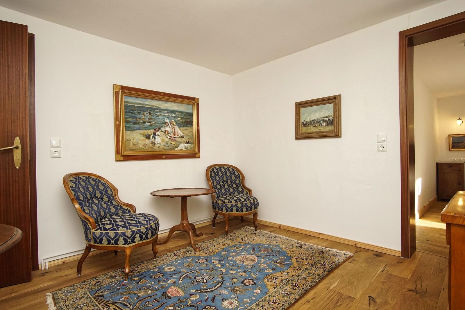 Zimmer mit zwei Stühlen, Tisch und Teppich. Wandbilder und Holzboden.