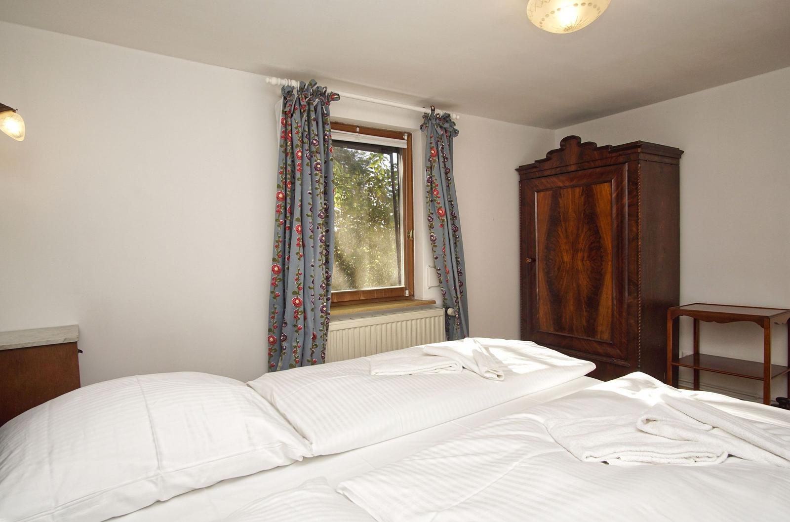 Schlafzimmer mit Bett, Kleiderschrank und Fenster mit Vorhängen.