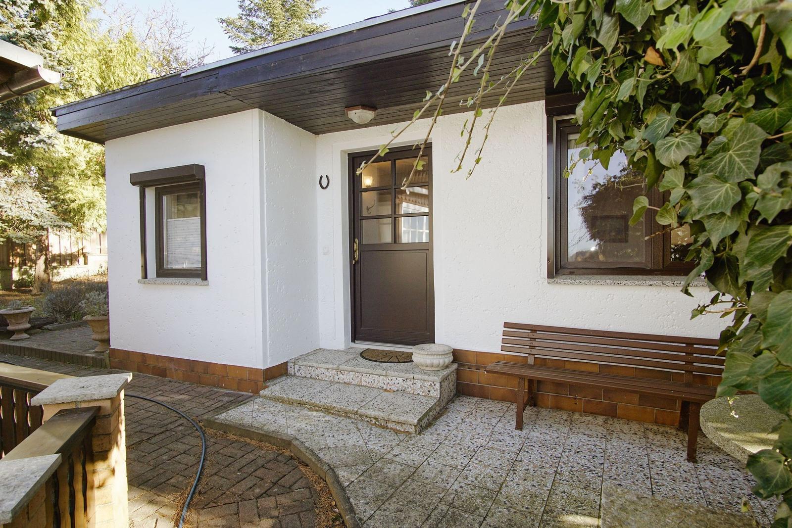 Eingangsbereich mit brauner Tür, Bank und Pflanzen.