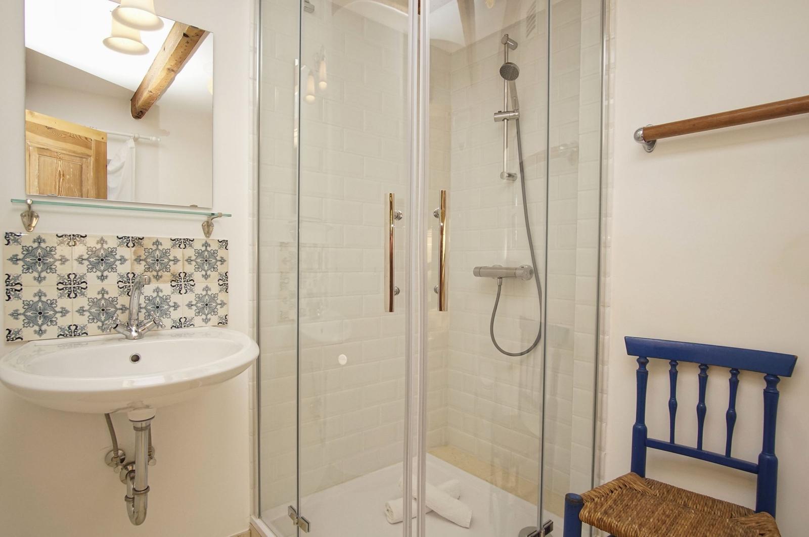 Bad mit Dusche, Waschbecken und blauer Stuhl.