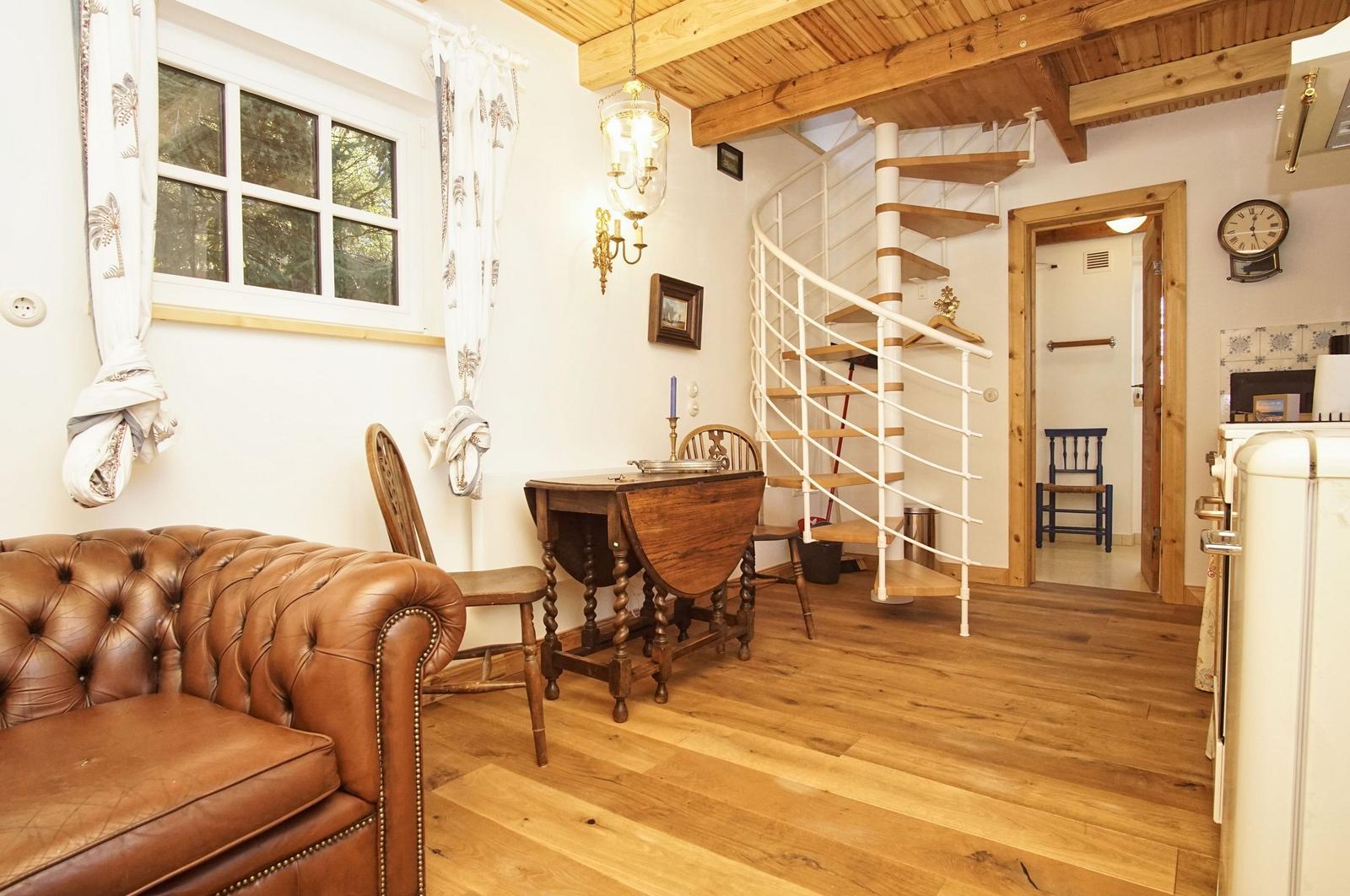 Wohnbereich mit braunem Ledersofa, Holztisch und Wendeltreppe.