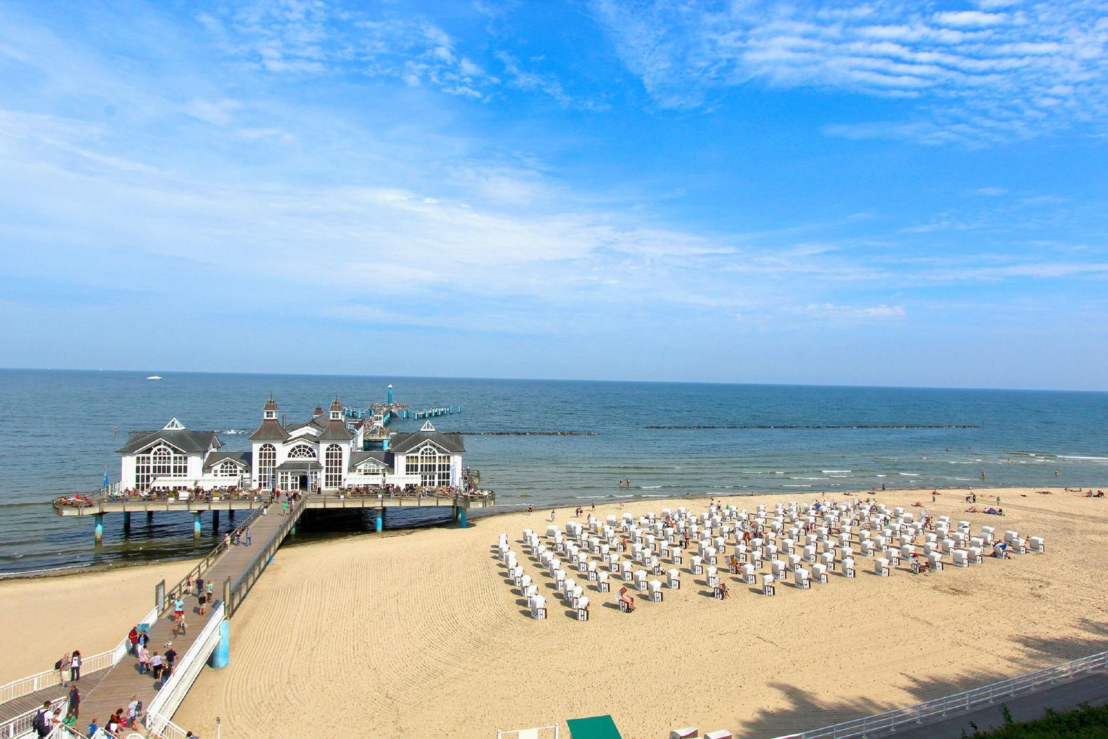 Strand mit Strandkörben, Pier und Meer unter blauem Himmel.