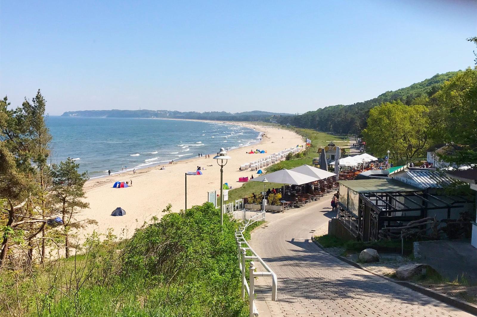 Strandpromenade mit Strand, Bäumen und Terrassenbereich.