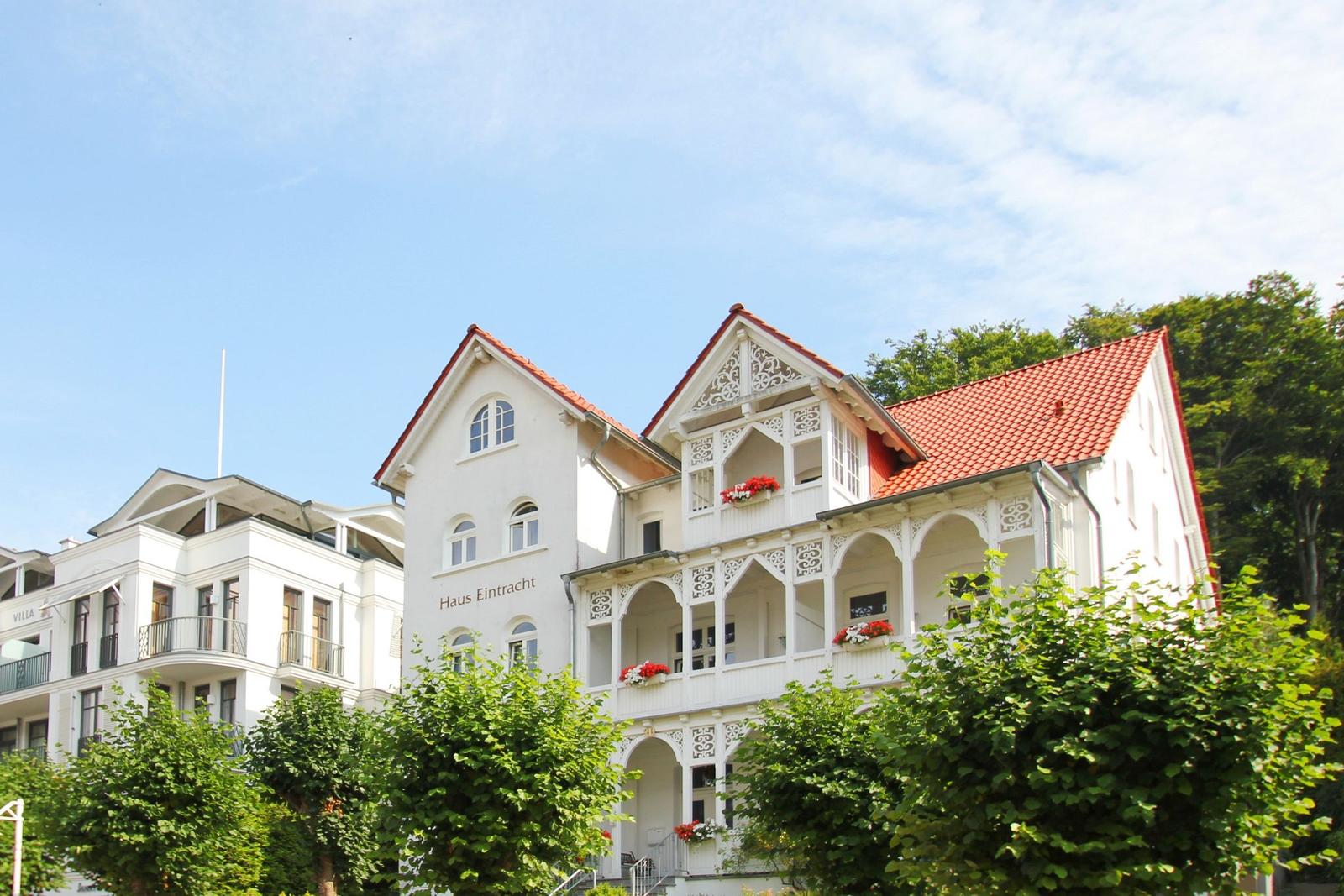 Weißes Haus mit rotem Dach und Balkonen mit Blumen.