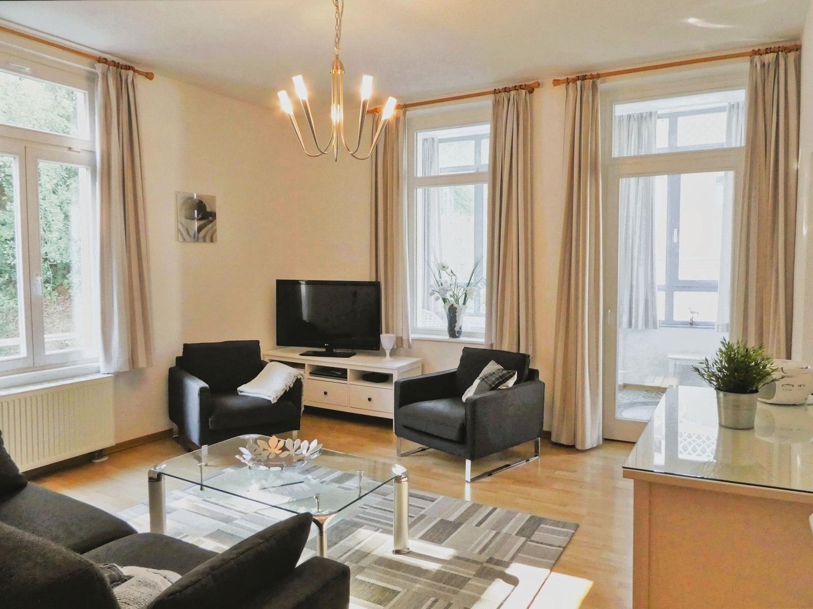 Wohnzimmer mit zwei Sesseln, Glas-Tisch und Fernseher.